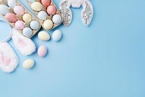 Pastel colored Easter eggs and bunny ears on blue background with copy space photo