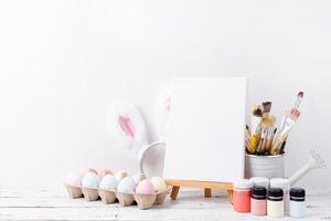 Pastel colored Easter eggs and mimosa flowers with blank white frame for mockup design, front view on white brick wall background photo