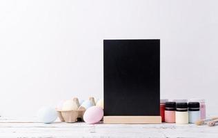 Pastel colored Easter eggs and mimosa flowers with blank white frame for mockup design, front view on white brick wall background photo