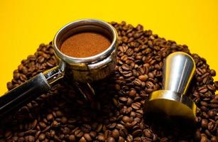 Coffee holder placed into coffee roasted beans on the yellow table in daylight photo