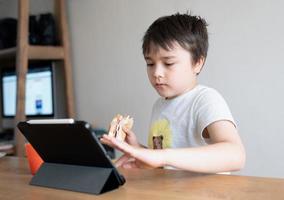 Kid eating eating homemade bacon sandwiches and watching cartoon on tablet, Child boy having  breakfast and playing game online on internet with friends before go to school in the morning photo