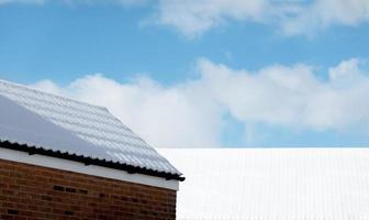 ladrillo casa con nieve en el embaldosado techo en invierno. hormiga ver exterior arquitectura de casa, garaje y cobertizo techo parte superior con nieve cubrir en contra azul cielo y nubes foto