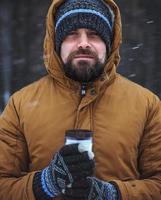 Beard man with hot drink in thermos cup in winter forest photo