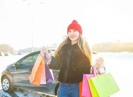sonriente caucásico mujer participación su compras bolso cerca el coche foto