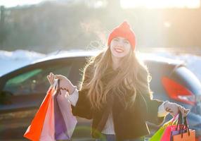 sonriente caucásico mujer participación su compras bolso cerca el coche foto