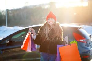 sonriente caucásico mujer participación su compras bolso cerca el coche foto