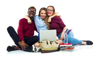 Tres contento estudiantes sentado con libros, ordenador portátil y pantalones foto