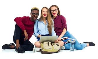 Tres contento estudiantes sentado con libros, ordenador portátil y pantalones foto