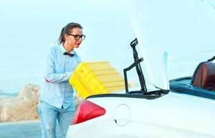 Woman loading luggage into the back of convertible car parked alongside the road photo