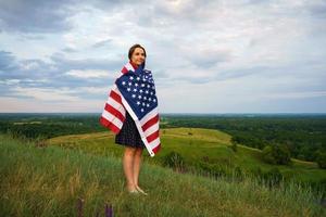 orgulloso mujer con un nosotros bandera es en pie en parte superior de un colina foto