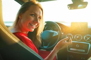Happy woman in a red dress with a key in her hand is sitting in the car photo