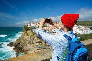 Woman with a backpack makes a photo on the smartphone of a beautiful panorama of the ocean coast near Azenhas do Mar, Portuga