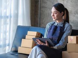 Asian female entrepreneur starting an online sales business using laptops, tablets, and smartphones to place orders and check products inside her own office, SME online concept. photo