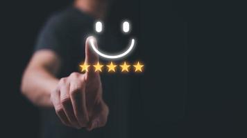 Customer service satisfaction survey concept.Business people or customers show satisfaction by pressing face emoticon smile give rating five stars in satisfaction on virtual touch screen. photo