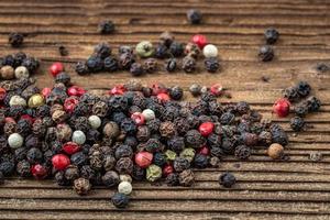 Peppercorns on dark rustic wooden background. Mix of different peppers photo