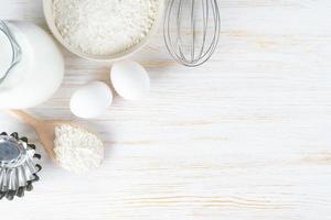 Baking ingredients flour, eggs, milk, bakeware on white wooden background with copy space photo