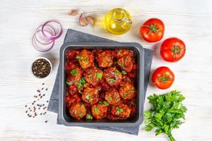 Homemade meatballs with tomato sauce and spices served in black pan on white wooden background photo