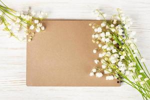 Bouquet of flowers lily of the valley and empty paper notebook on white rustic table. photo