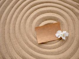 Letter in the sand. Craft paper with a white flower on the texture of sea sand. Concept of a beach holiday photo