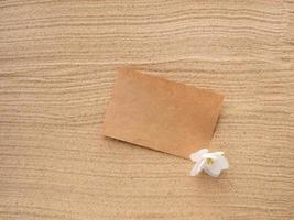 Letter in the sand. Craft paper with a white purple flower on the texture of sea sand. Concept of a beach holiday photo