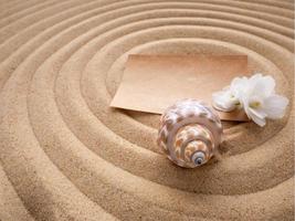 Craft paper letter with a white flower and a shell on the sand in the form of a spiral. The concept of a beach holiday photo