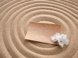 Letter in the sand. Craft paper with a white flower on the texture of sea sand. Concept of a beach holiday photo