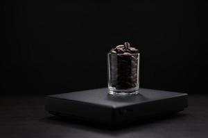 Dark roasted coffee beans in a clear glass on a black digital scale. photo