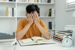 asiático estudiante hombre tener ansiedad porque de exámenes, masculino preparar para prueba y aprendizaje lecciones en el biblioteca. estrés, desesperación, prisa, malentendido lectura, desanimado, expectativa, conocimiento foto