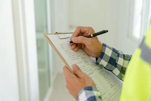 el inspector o ingeniero está inspeccionando la construcción y el aseguramiento de la calidad de la nueva casa usando una lista de verificación. ingenieros o arquitectos o contratistas trabajan para construir la casa antes de entregársela al propietario foto