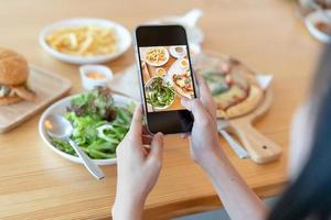 mujer toma una foto de una comida en la mesa después de pedir comida en línea para comer en casa. fotografía y uso de conceptos de teléfono