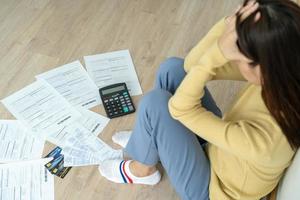 mujer asiática estresada y con dolor de cabeza con grandes facturas o facturas sin dinero para pagar los gastos y la deuda de la tarjeta de crédito. escasez, problemas financieros, hipoteca, préstamo, bancarrota, en quiebra, pobre, billetera vacía foto