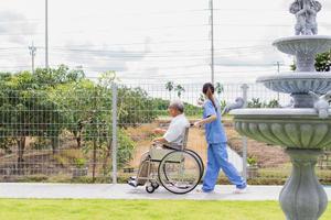 enfermería hogar cuidado concepto. asiático joven enfermero discapacitado mayor hombre. enfermero, cuidado hogar y mayor hombre con invalidez en un silla de ruedas en un fuera de médico instalación. foto