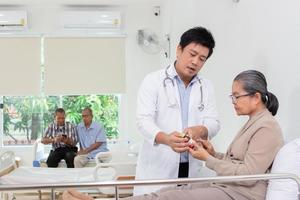 Asian male doctor explaining medicine to elderly female patient in hospital. photo