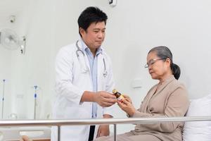 asiático masculino médico explicando medicina a mayor hembra paciente en hospital. foto