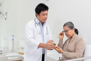 Asian male doctor explaining medicine to elderly female patient in hospital. photo