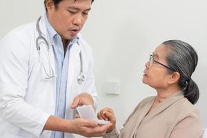 asiático masculino médico explicando medicina a mayor hembra paciente en hospital. foto