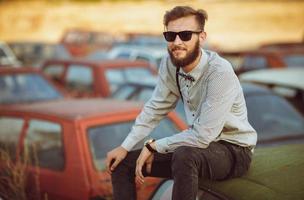 joven hermoso elegante hombre, vistiendo camisa y corbata de moño en el campo de antiguo carros foto