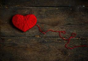 Red heart shape made from wool on old shabby wooden background photo