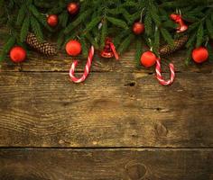 Borde de Navidad con ramas de abeto, conos, adornos navideños y bastón de caramelo sobre tablas de madera rústica foto