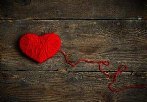 Red heart shape made from wool on old shabby wooden background photo