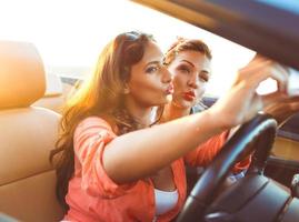 dos joven hermosa muchachas son haciendo selfie en un convertible foto