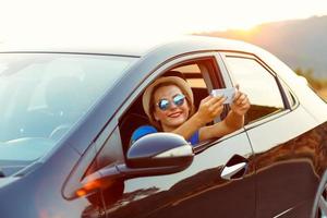 mujer en sombrero y Gafas de sol haciendo yo retrato sentado en el coche foto