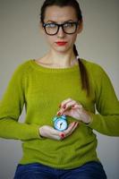 Little blue alarm clock in the hands of pensive young woman photo