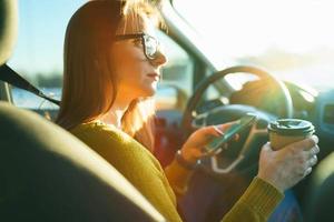Woman using smartphone and drinking coffee while sitting in a car photo