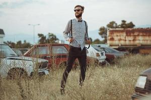 joven hermoso elegante hombre, vistiendo camisa y corbata de moño en el campo de antiguo carros foto