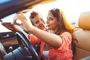 dos joven hermosa muchachas son haciendo selfie en un convertible foto