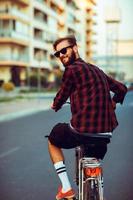 elegante hombre en Gafas de sol montando un bicicleta en ciudad calle foto