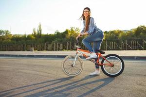 Lovely young woman in a hat riding a bicycle on city background in the sunlight outdoor photo