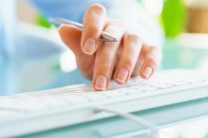 Woman office worker with pen in hand typing on the keyboard photo