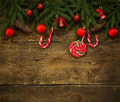 Borde de Navidad con ramas de abeto, conos, adornos navideños y bastón de caramelo sobre tablas de madera rústica foto